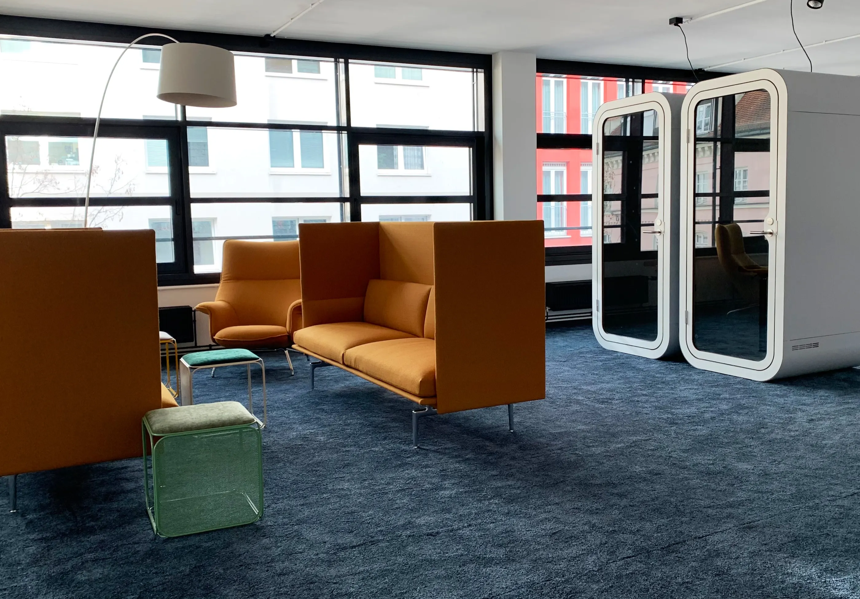 Lounge mit orangefarbenen Highback-Sofas, blauem Teppich und zwei Telefonboxen