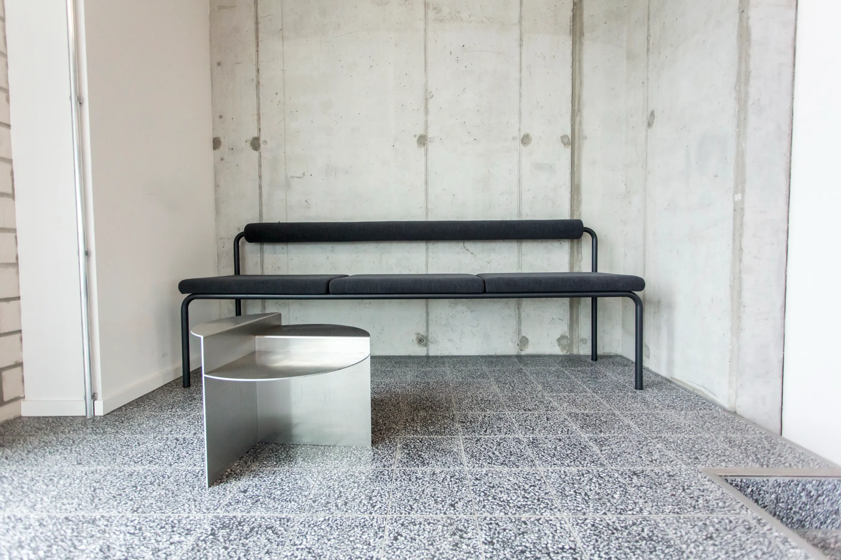 Lobby mit Sichtbetonwand, Terrazzoboden und einer langen schwarzen Bank
