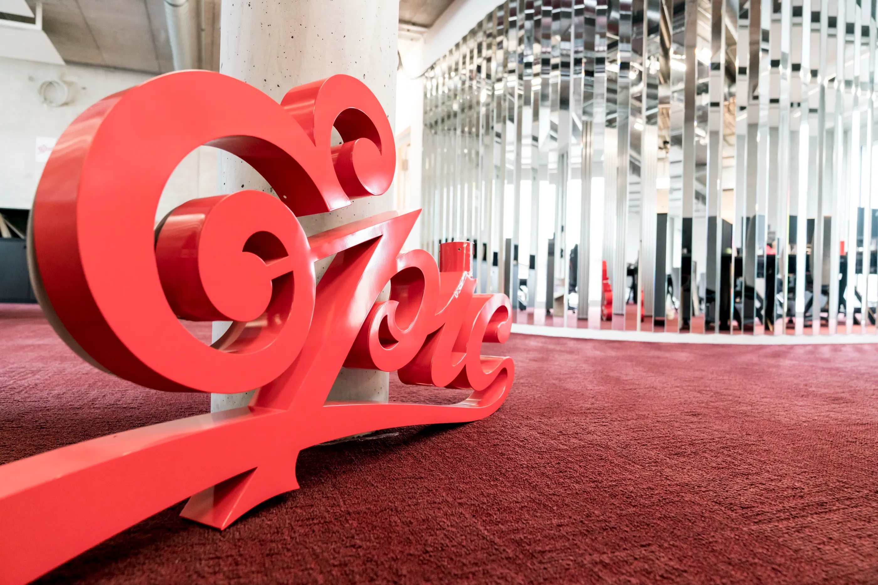 Rote Schriftskulptur auf der Bürofläche, dahinter eine verspiegelte Decke