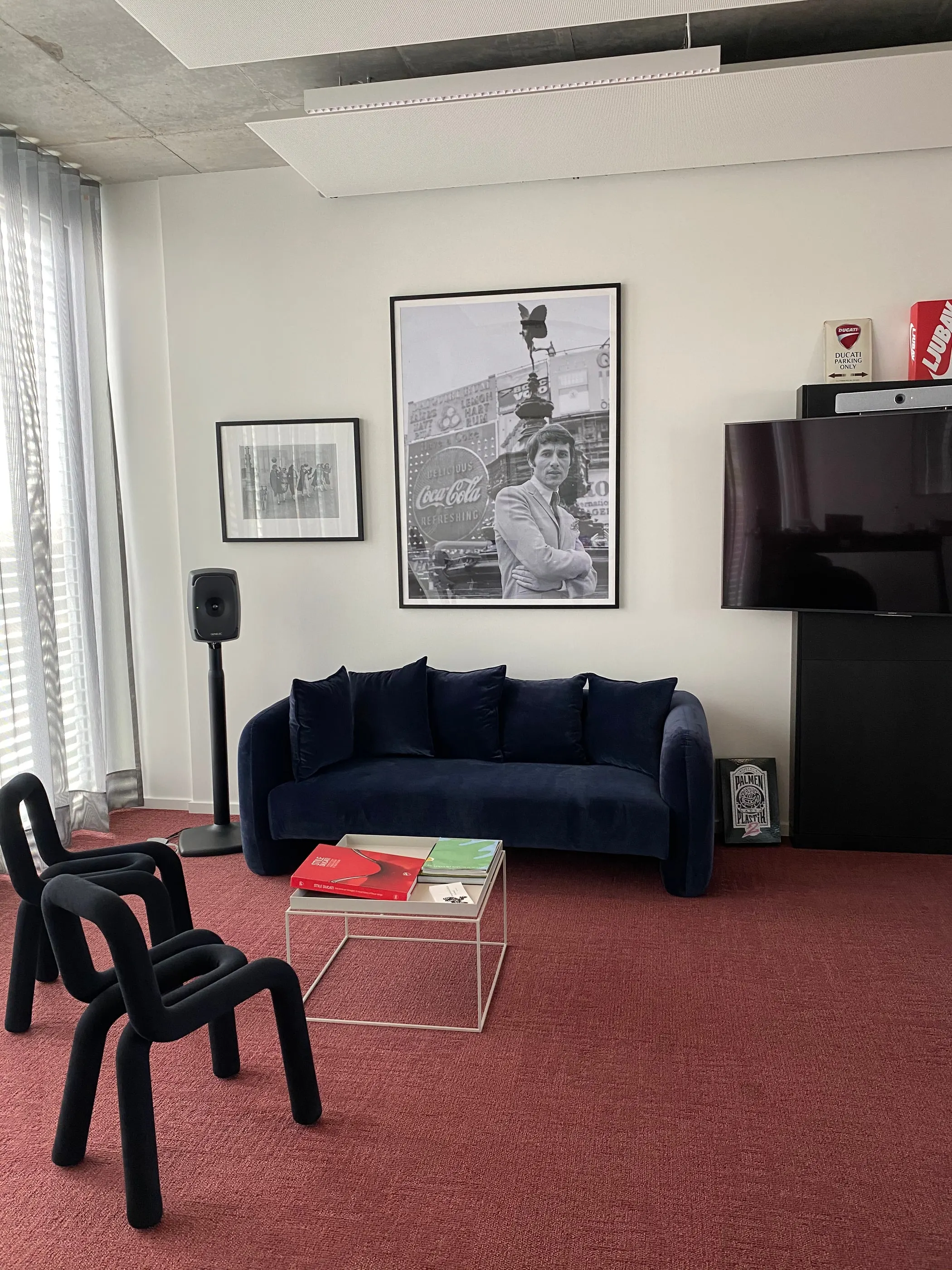 Besprechungsecke mit dunkelblauem Sofa, Wandbildschirm und gerahmtem Schwarz-Weiß-Porträt
